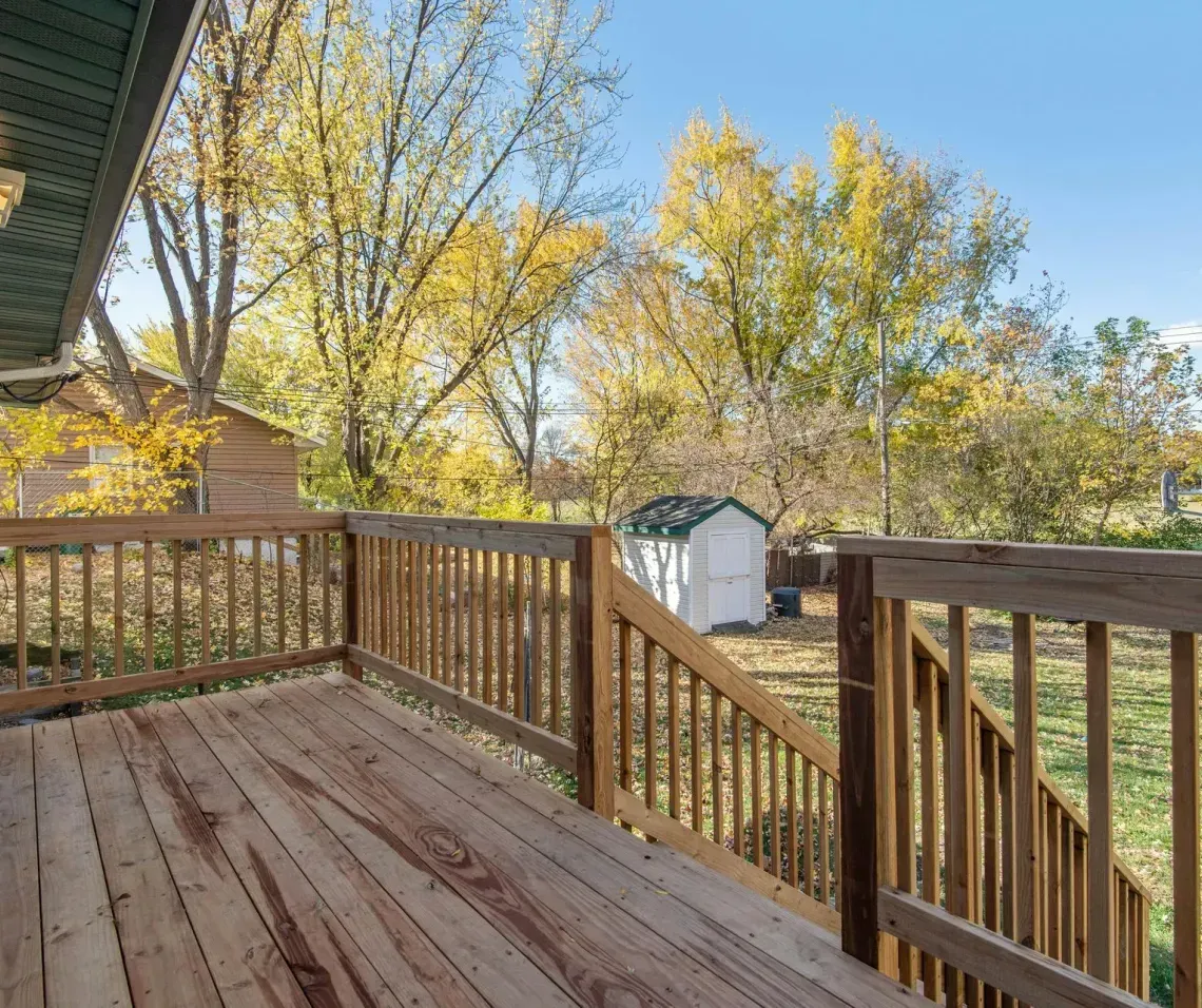 Wooden back deck with railings overlooking a yard and autumn trees under a blue sky