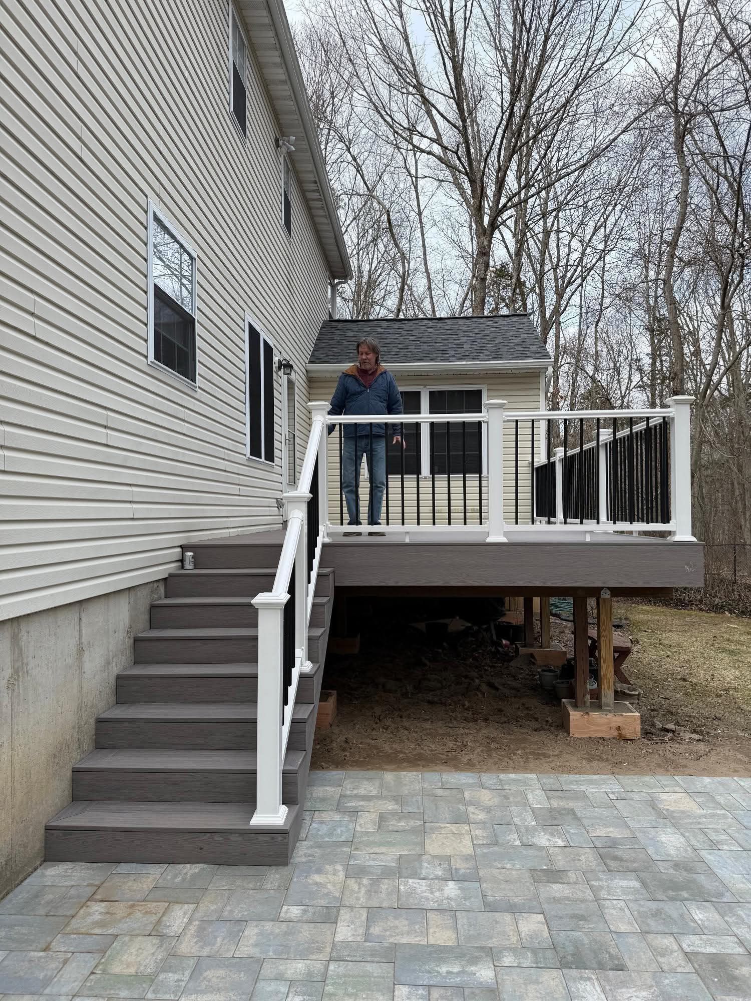 Person standing on a raised wooden deck beside a house with stairs and white railing