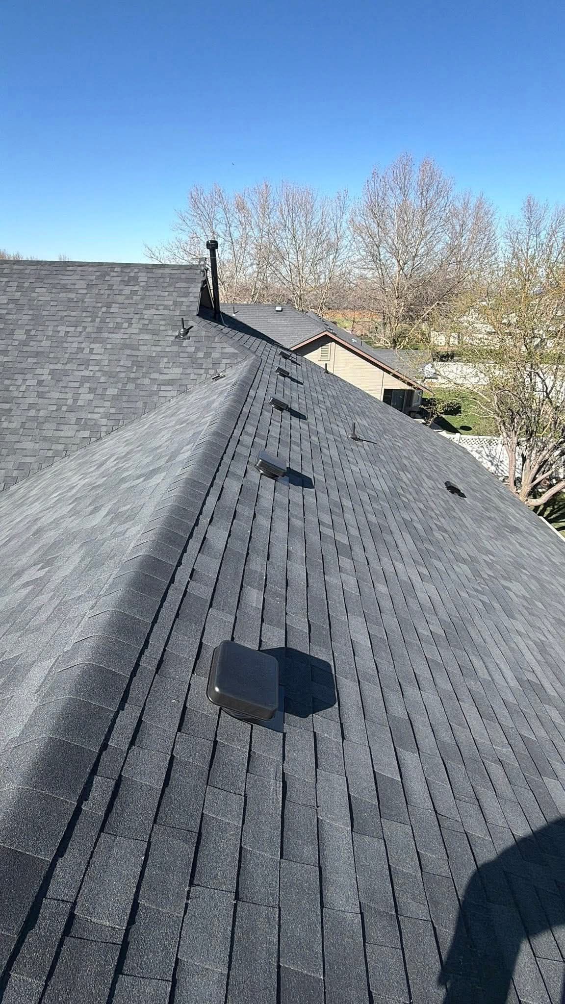Roof shingles with a vent pipe under a clear blue sky, viewed from the roofline.