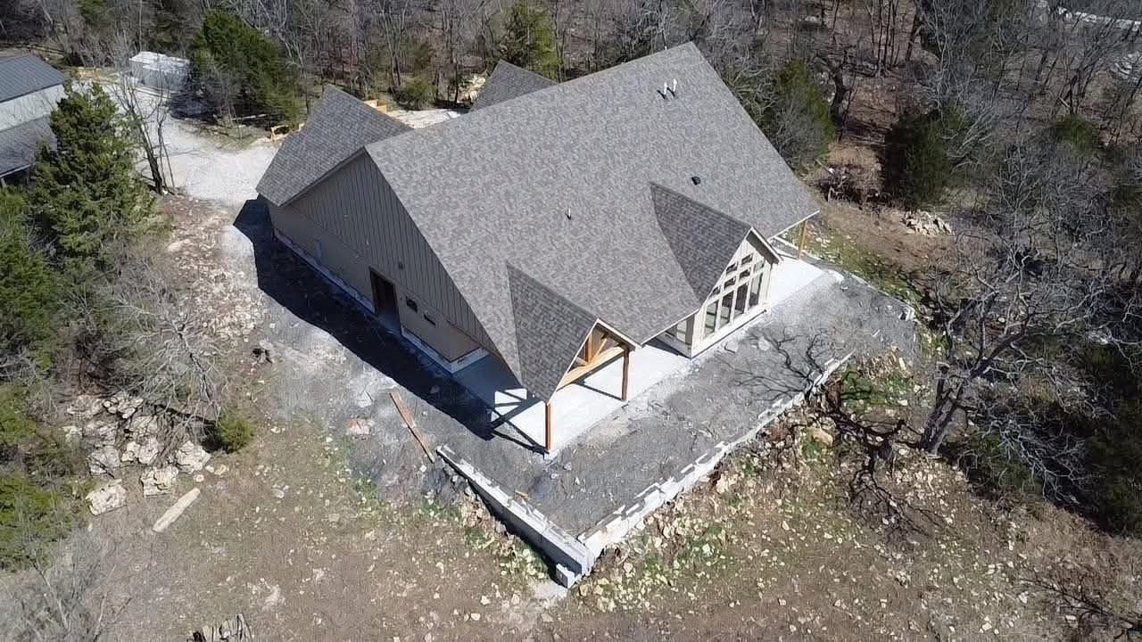 Aerial view of a gray-roofed house surrounded by trees and rocky ground