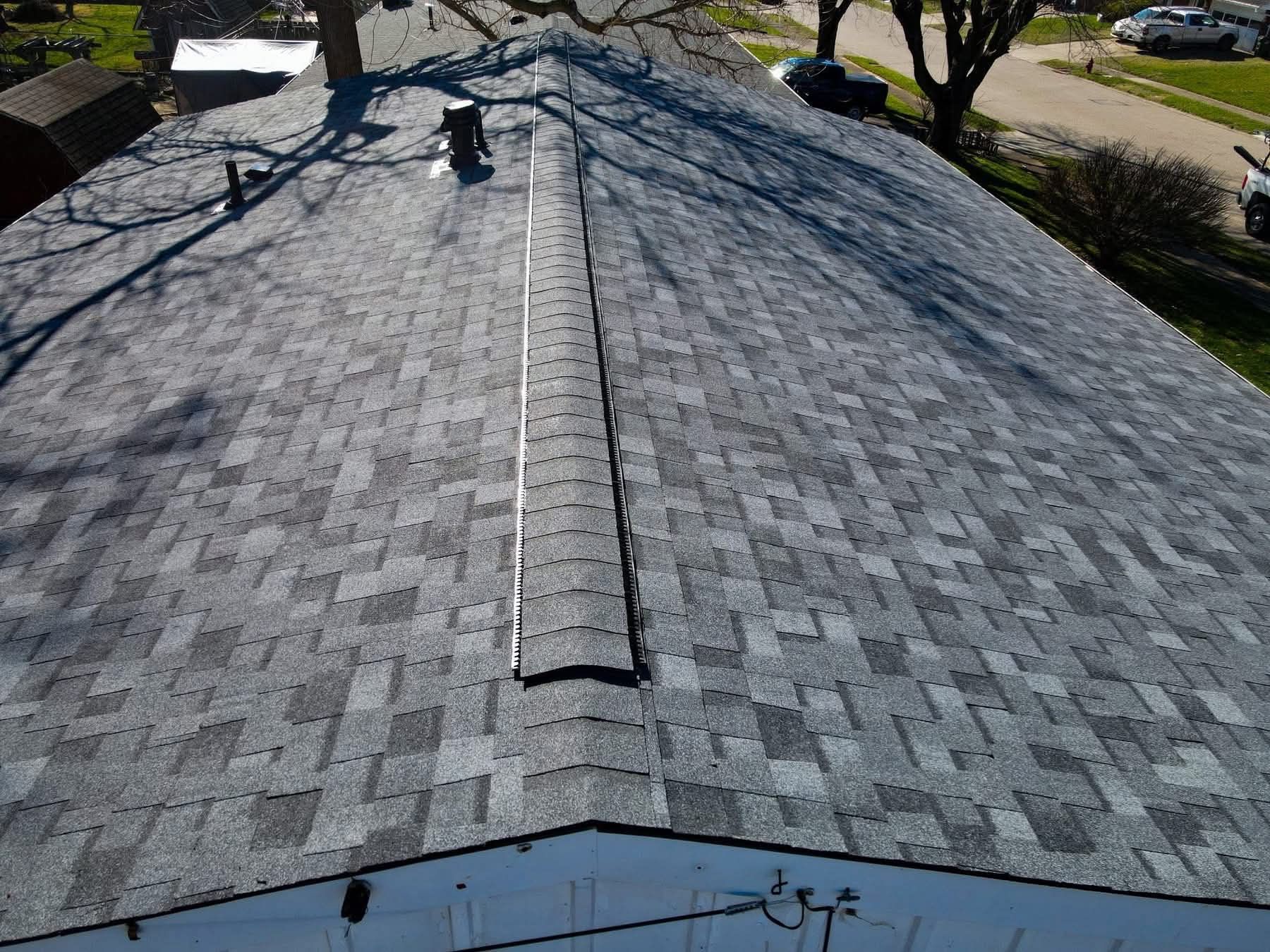 Gray shingled roof with a central ridge vent, viewed from above after repair or inspection