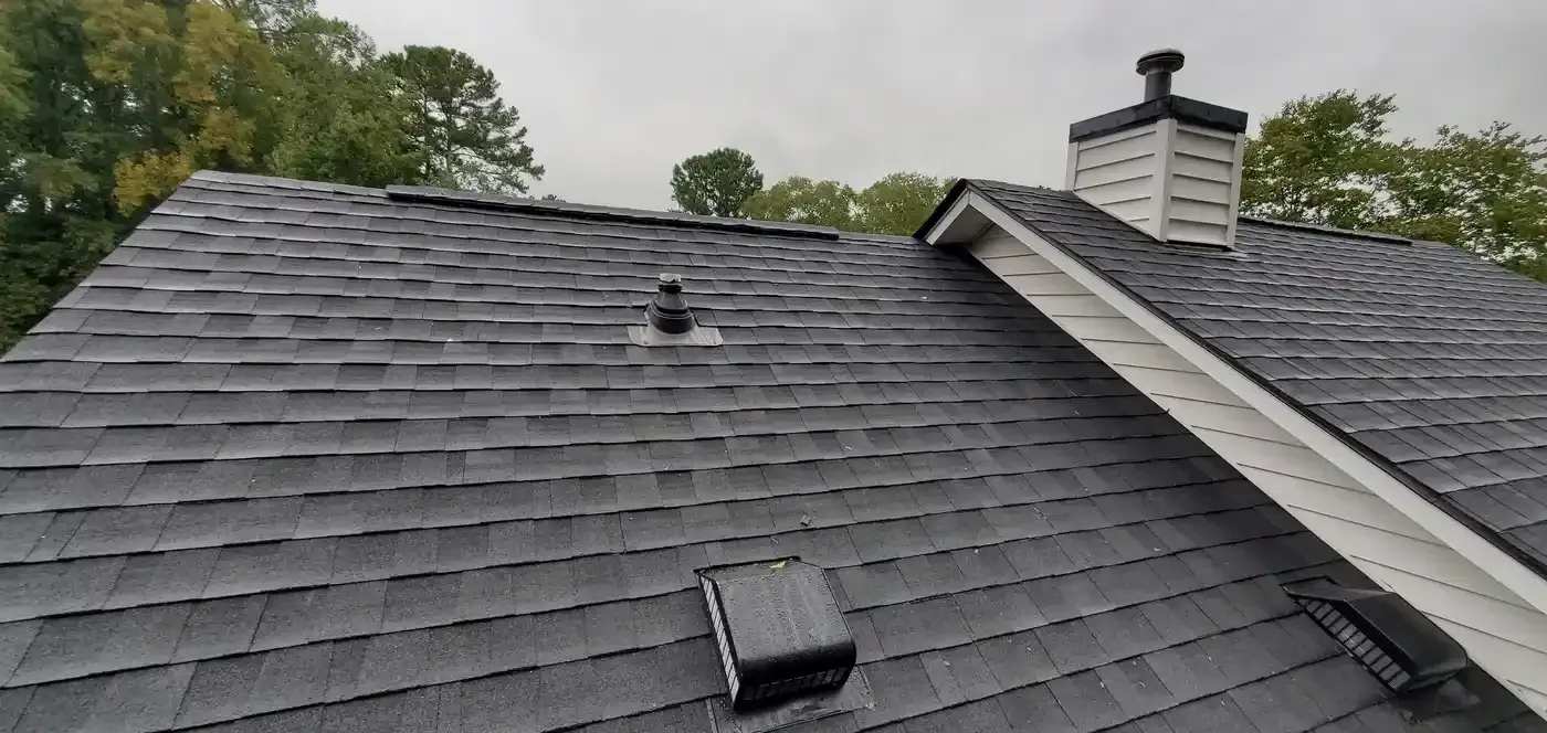Shingled roof with vent pipe and chimney under overcast sky, viewed from above