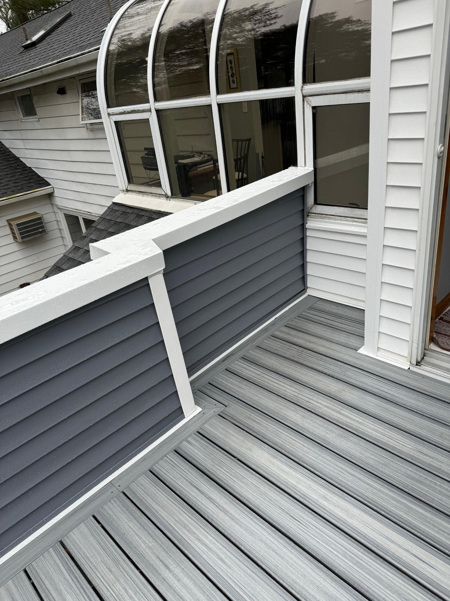Gray rooftop deck with white railing and curved window, viewed from above
