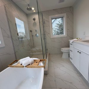 Modern white bathroom with soaking tub, glass shower, vanity, and toilet under bright recessed lights