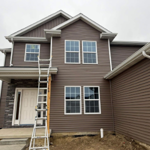 Two-story brown house with white trim and a ladder leaning against the front porch.