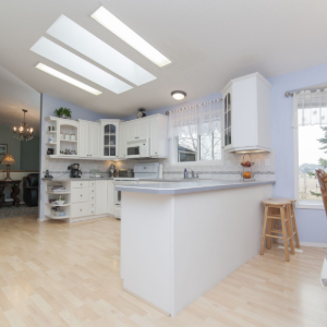 Bright, modern white kitchen with island, skylights, and dining area by sliding glass doors