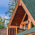 Wooden cabin with green roof among tall pine trees under a clear blue sky