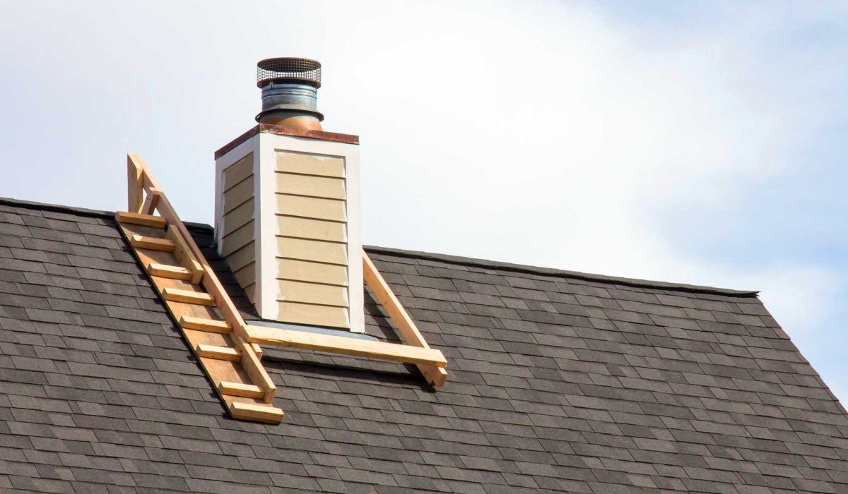 Ladder leaning against a roof beside a chimney with a metal cap under a bright sky