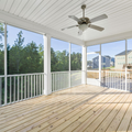 Covered wooden porch with white railings, ceiling fan, and view of neighboring houses and trees