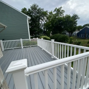 White wooden deck with railings beside a green house on a cloudy day