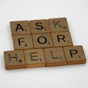 Wooden letter tiles spelling “ASK FOR HELP” on a white background