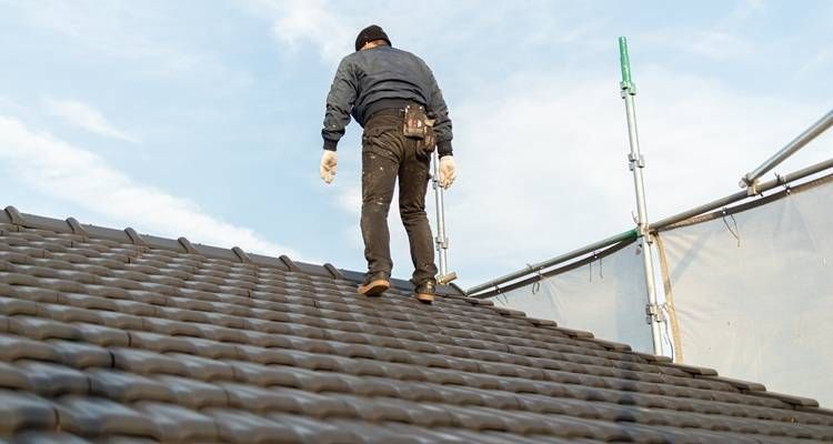 Worker standing on a sloped roof near scaffolding, inspecting roofing tiles.
