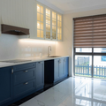 Modern kitchen with blue cabinets, white countertops, and a window with a brown blind.