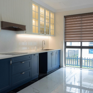 Modern kitchen with blue cabinets, white countertops, and a window with a brown blind.