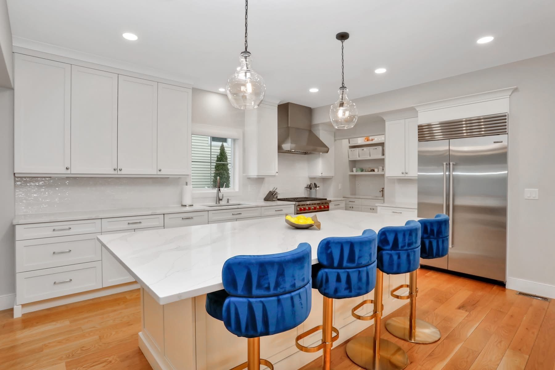 Modern white kitchen with island, stainless steel appliances, and three blue bar stools