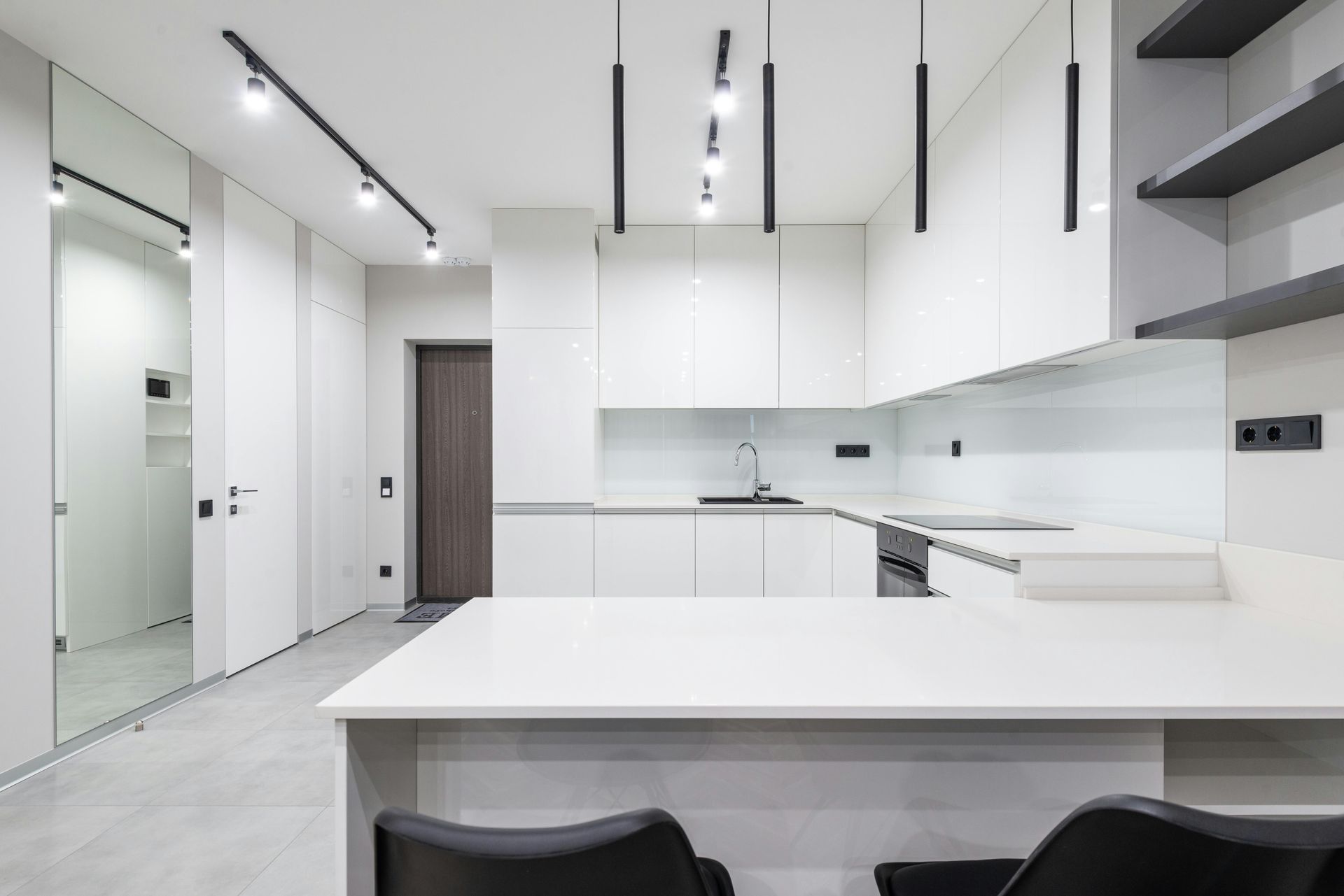 Modern white minimalist kitchen with glossy cabinets, island, black chairs, and track lighting