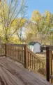 Wooden backyard deck with railings, autumn trees, and a small shed in the yard.