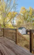 Wooden backyard deck with railings, autumn trees, and a small shed in the yard.