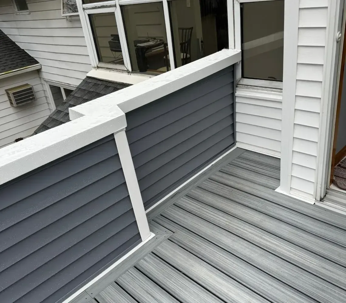 Gray rooftop deck with white railing and curved window, viewed from above