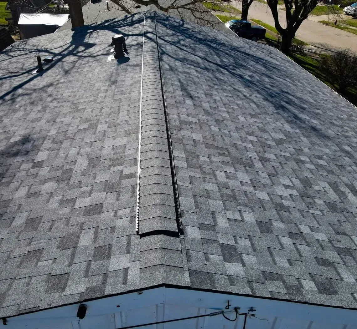 Gray shingled roof with a central ridge vent, viewed from above after repair or inspection