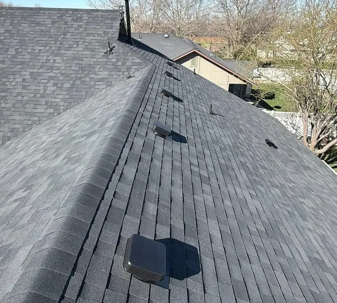 Roof shingles with a vent pipe under a clear blue sky, viewed from the roofline.