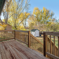 Wooden backyard deck with railings, autumn trees, and a small shed in the yard.