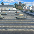 Rooftop with several skylights and two workers in the distance under a blue sky.