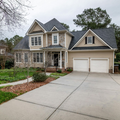 Two-story suburban house with a double garage and wide concrete driveway, surrounded by trees and lawn