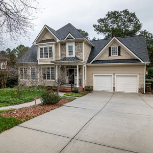 Two-story suburban house with a double garage and wide concrete driveway, surrounded by trees and lawn