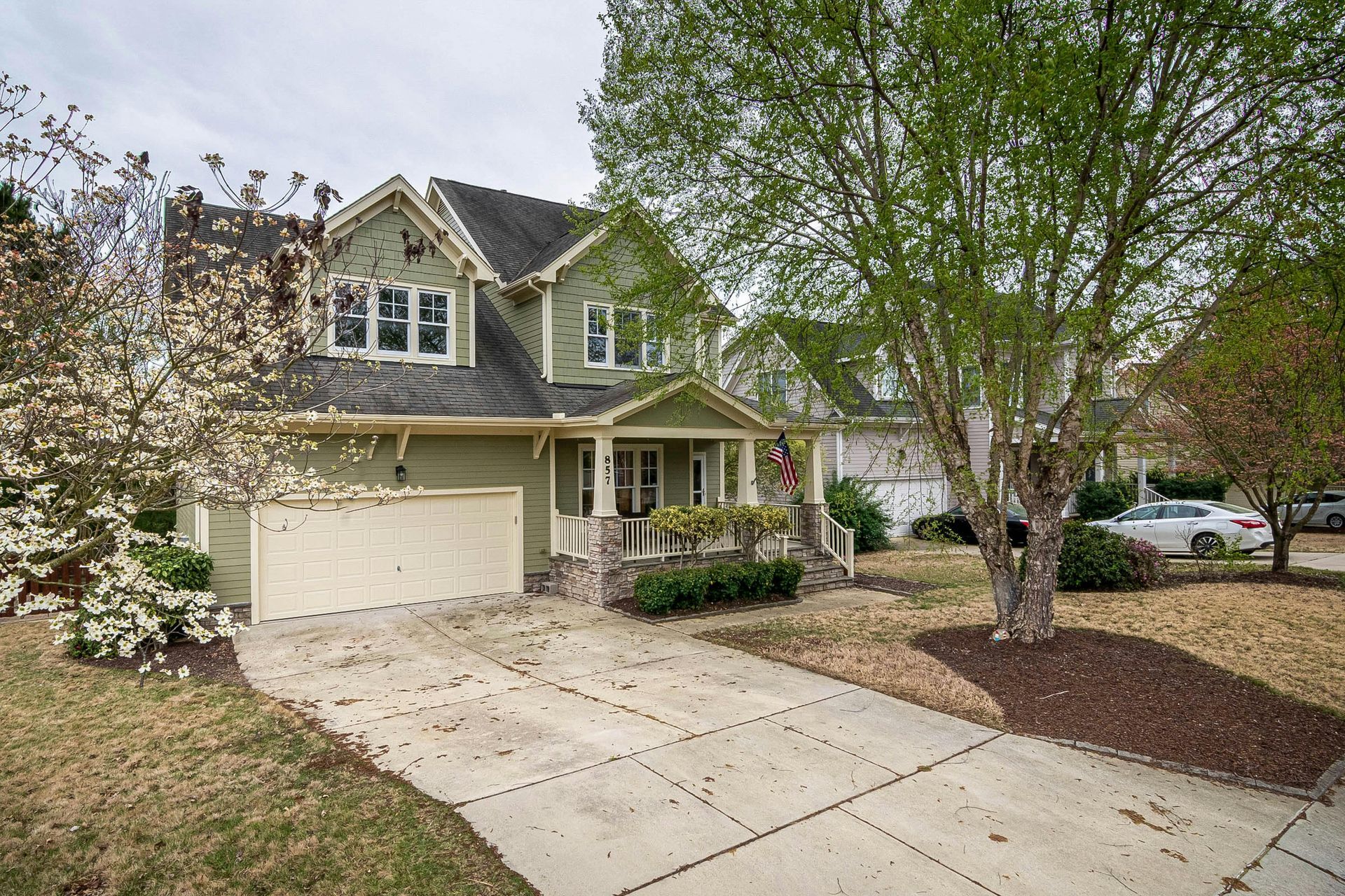 Suburban two-story house with beige garage, front porch, and a tree-lined driveway