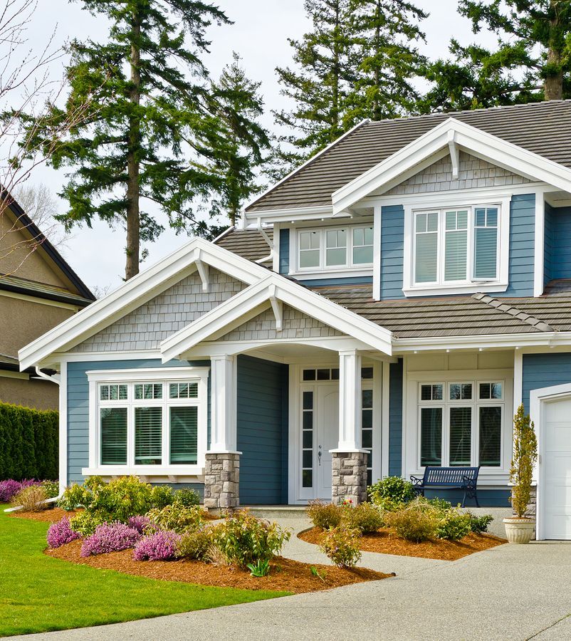 Suburban two-story blue house with white trim, front porch, landscaped garden, and driveway