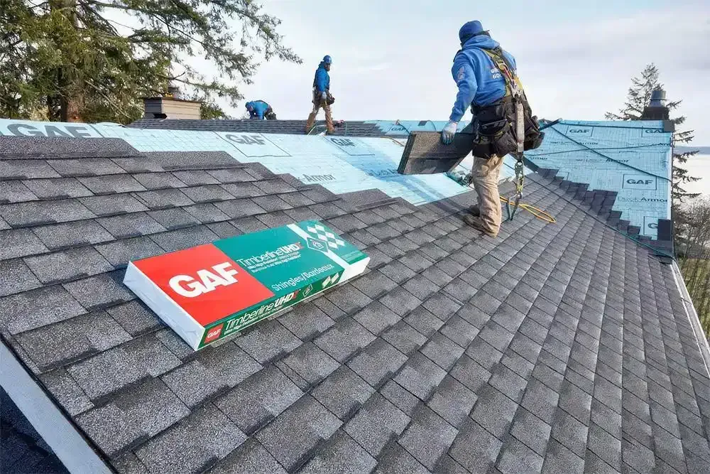 Workers installing blue shingles on a sloped roof, with a GAF roofing package in the foreground.