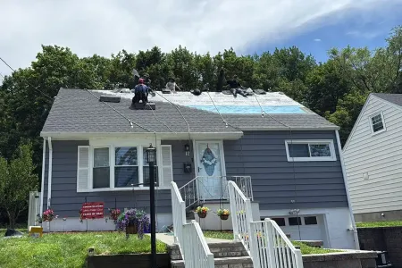 Damaged gray house with a tarp-covered roof, workers on top, and front steps leading to the entrance