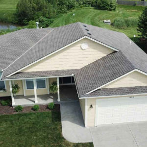 Aerial view of a single-story suburban house with a two-car garage and gray roof, surrounded by green lawn.