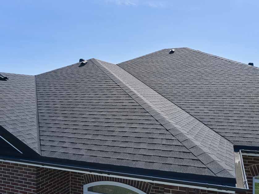 Dark gray shingled roof with a central ridge vent on a brick house