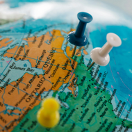 Pins on a globe marking locations in North America, with blue, white, and yellow pushpins.