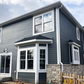 Gray two-story house with white trim and stone accents under a cloudy sky