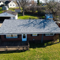 Aerial view of a red brick house with a gray roof, wooden deck, and green yard.