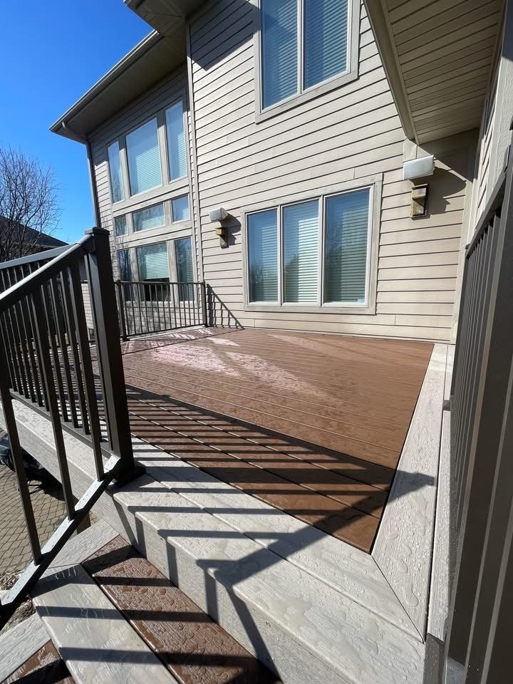 Backyard deck with beige siding, sliding glass doors, and black railing in sunlight