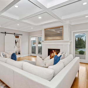 Bright living room with white sectional sofa, fireplace, and large glass doors overlooking trees