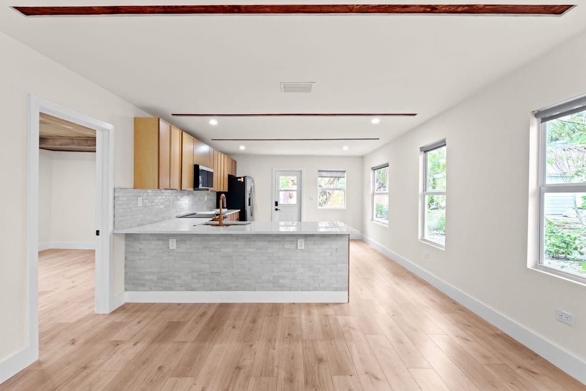 Bright open kitchen with light wood floors, gray island, and large windows in a modern home.