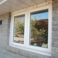 White-framed window in a gray brick house wall beside a porch light.