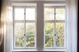 Bright window with white curtains and sunlight filtering through trees outside