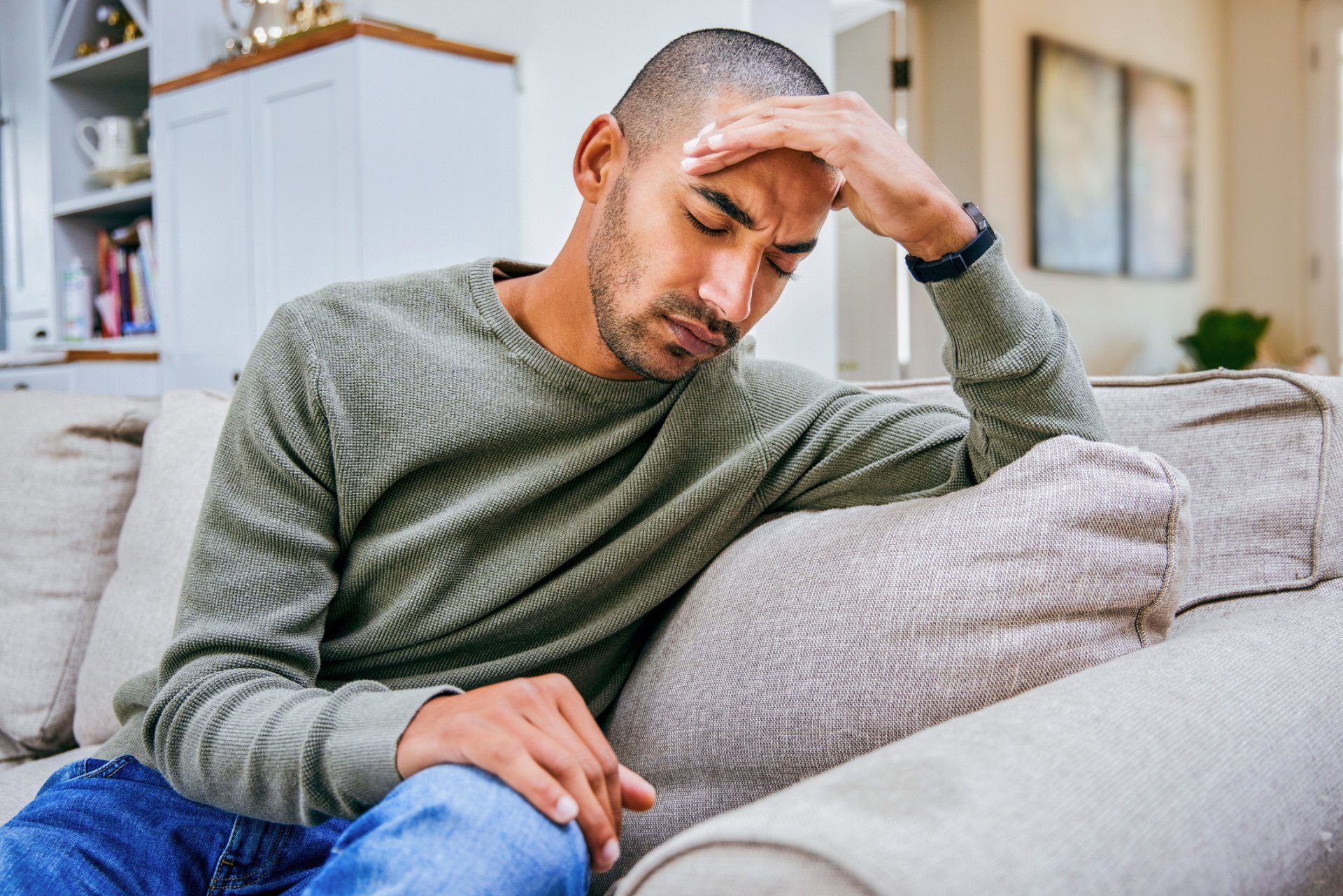 a man sitting on a couch with his hand on his forehead