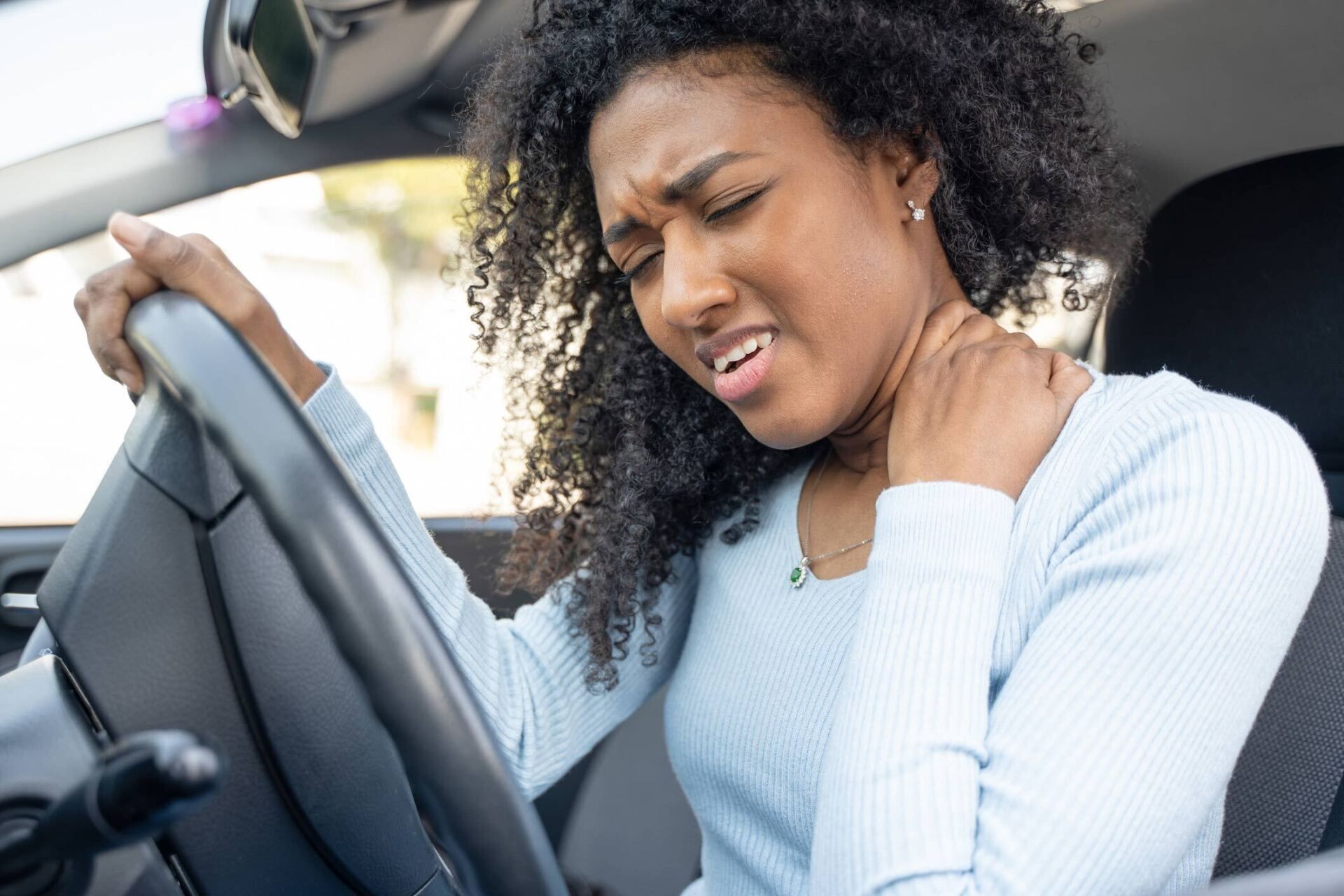 a woman is sitting in a car holding her neck in pain