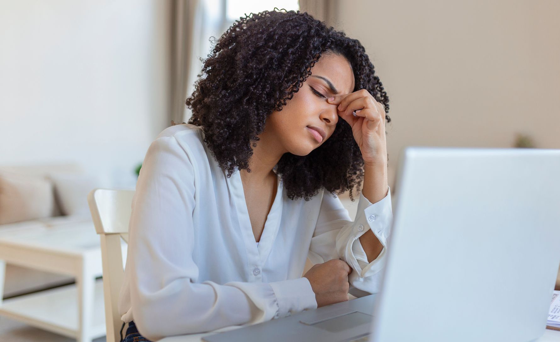 An African American woman sits in front of a laptop, she pinches the bridge of her nose in annoyance, she does not yet know the reasons to hire a life coach