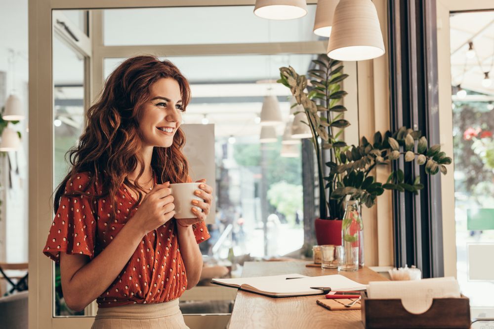 A woman is sitting at a table holding a cup of coffee.