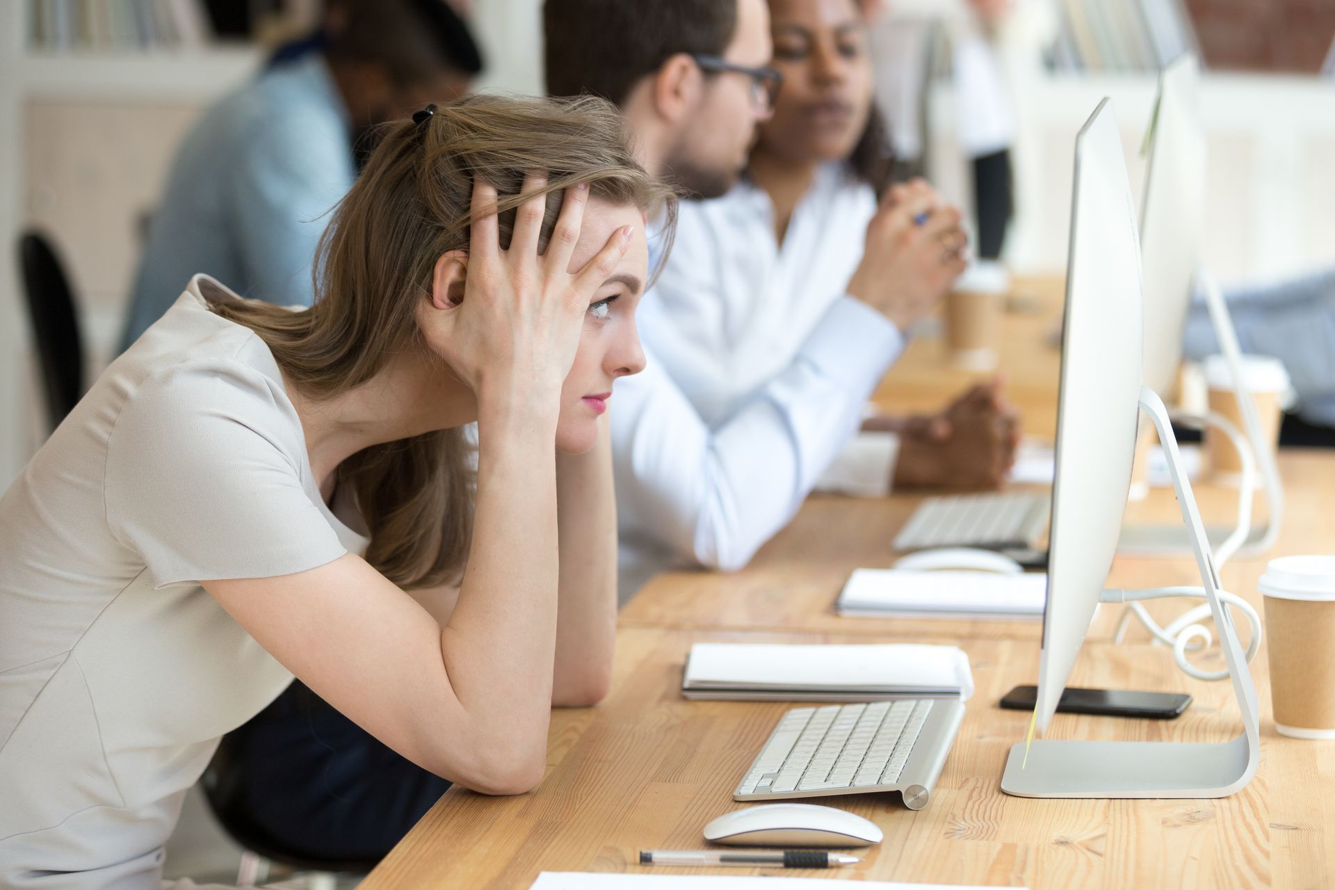 woman sitting at her computer at work with her hands holding her head stressed -- she is overthinking