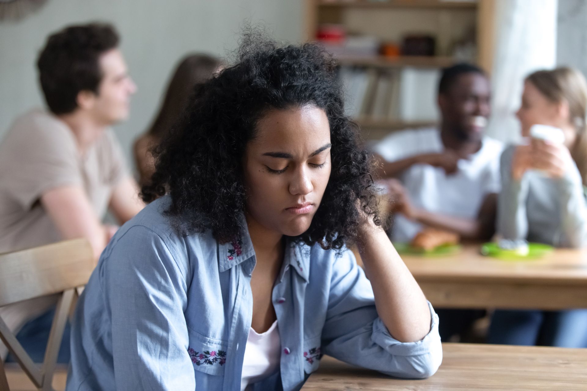 A young black woman sits away from a group of friends, she feels outcasted but is learning how to be herself around others