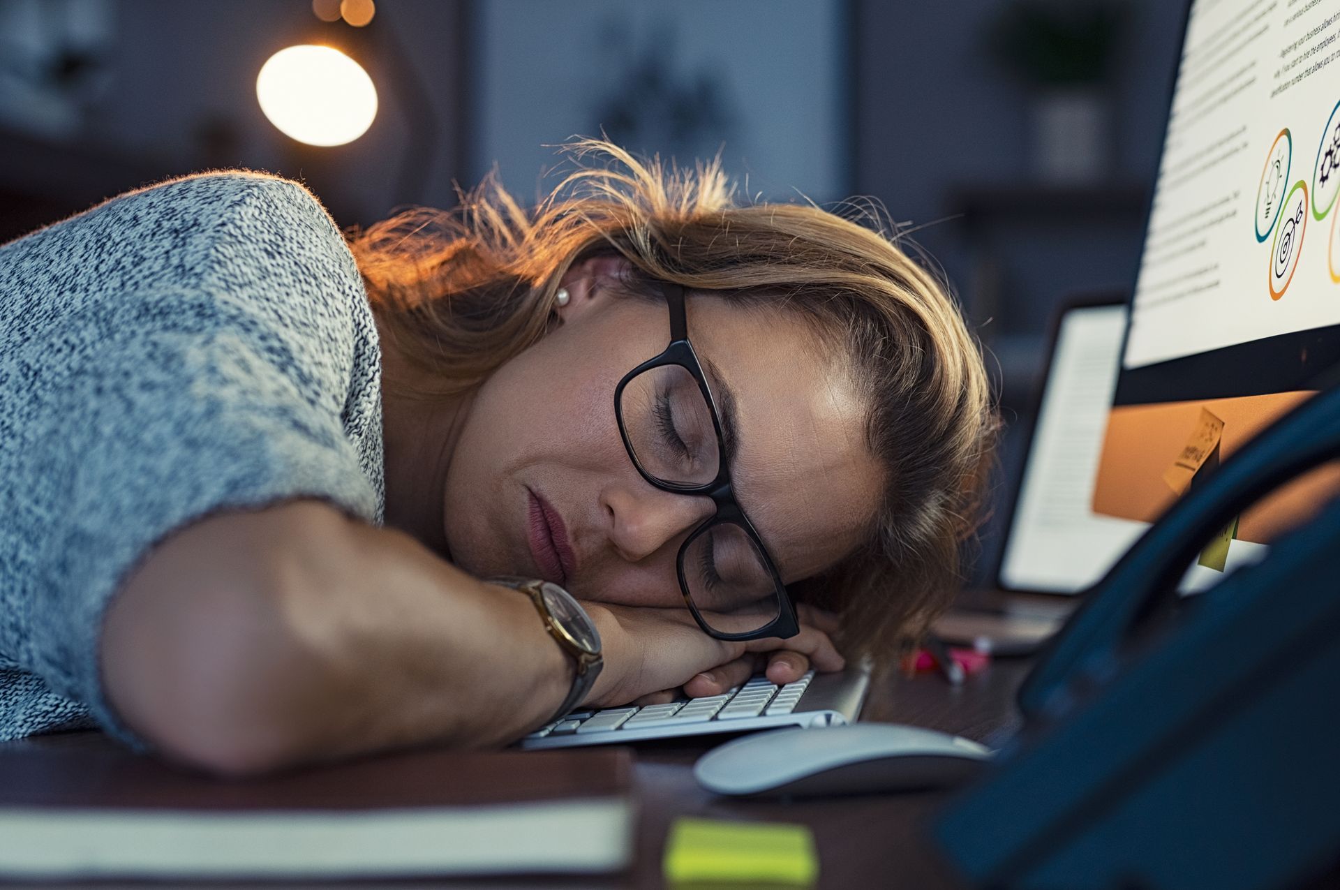 The same woman has fallen asleep at her desk, a symptom of her burnout